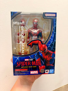 A hand holding a packaged Sh Figuarts Spider-Man action figure by Bandai Namco and Marvel. The box features Spider-Man artwork and the text 'Spider-Man Brand New Day'.