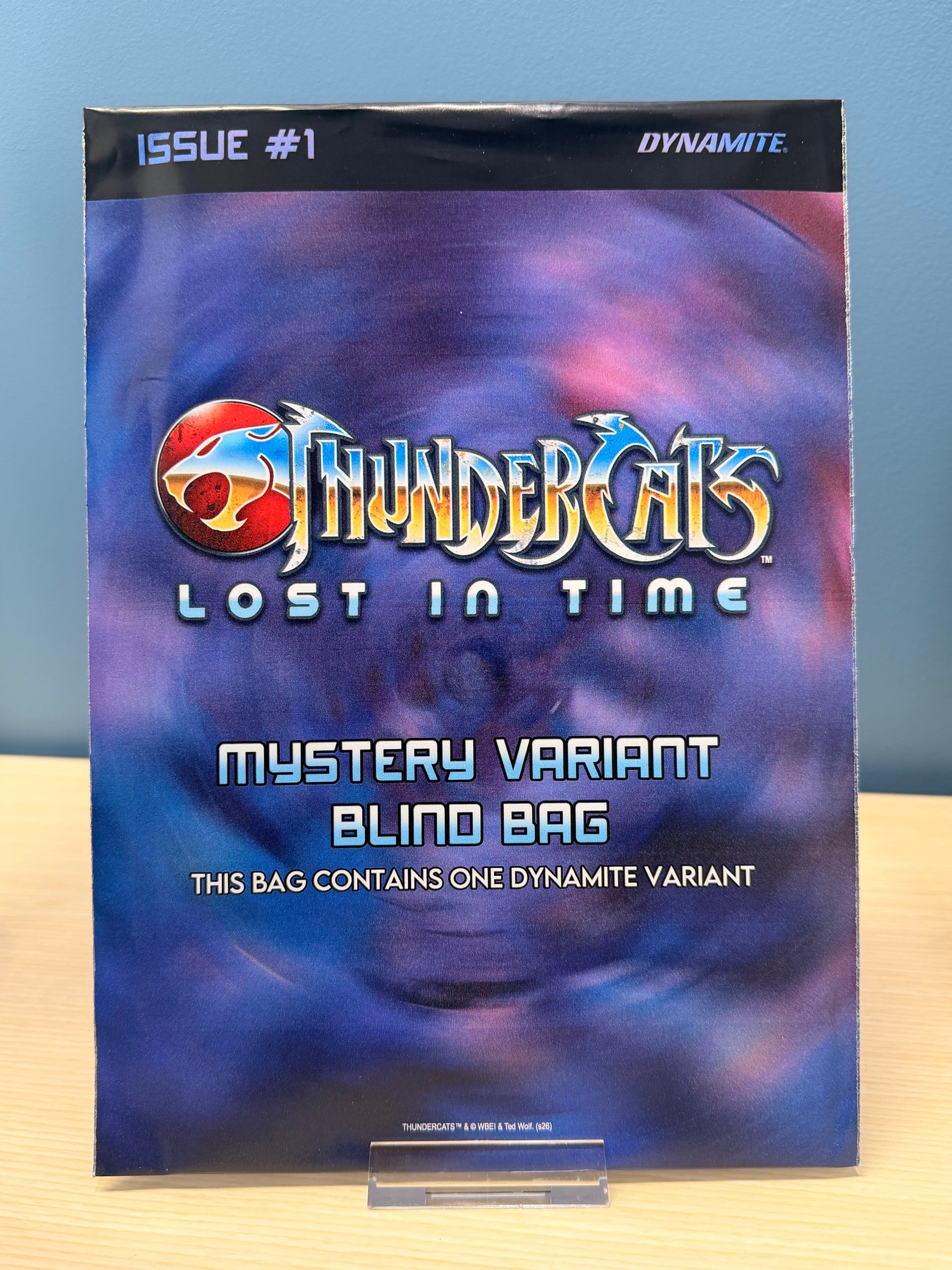 A comic book or magazine issue titled ThunderCats Lost in Time, Issue #1, with a 'Mystery Variant Blind Bag' label on the cover, photographed standing on a clear display stand against a blue wall and light wood surface.